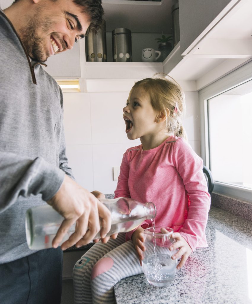 happy-man-pouring-water-glass-while-girl-sitting-kitchen-counter